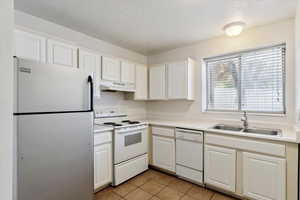 Kitchen with white appliances, light countertops, a textured ceiling, light tile patterned flooring, and white cabinetry