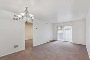 Carpeted empty room with a textured ceiling and hanging lights