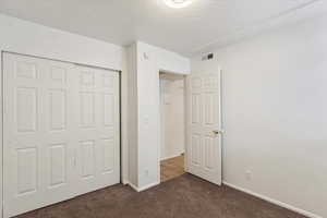 Unfurnished bedroom with a closet, a textured ceiling, and dark carpet