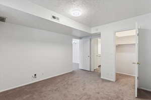 Unfurnished bedroom featuring a spacious closet, light carpet, and a textured ceiling
