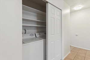Laundry area featuring a textured ceiling, light tile patterned floors, and washing machine and dryer