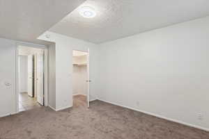 Unfurnished bedroom featuring a textured ceiling, carpet, and a walk in closet