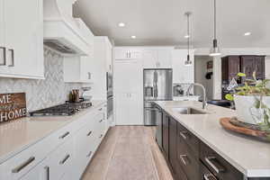 Kitchen with light stone counters, pendant lighting, stainless steel appliances, backsplash, and dual tone cabinets