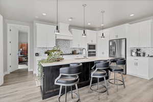 Kitchen featuring decorative light fixtures, stainless steel appliances, a kitchen island with sink, a breakfast bar area, and light wood-type flooring