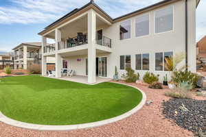 Back of property featuring stucco siding, a patio, a balcony, and a yard