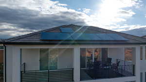 Rear view of house with stucco siding, roof mounted solar panels, outdoor dining space, and a tile roof