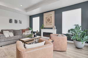 Living area with light wood finished floors, a glass covered fireplace, a tray ceiling, and recessed lighting