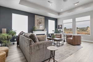 Living area with a raised ceiling, light wood-type flooring, a fireplace, recessed lighting, and a ceiling fan