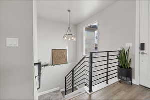 Staircase with wood finished floors and hanging lights