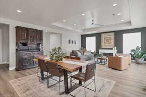 Dining area featuring a ceiling fan, a fireplace, light wood finished floors, recessed lighting, and a tray ceiling
