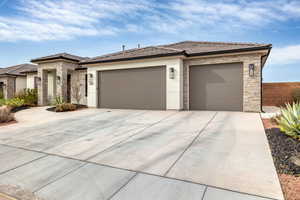 Prairie-style house featuring a tile roof, stone siding, driveway, and stucco siding