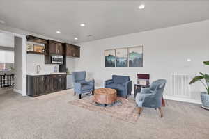 Living room with light carpet, bar with sink, and recessed lighting