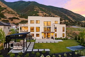 Back of house at dusk featuring a patio area, a mountain view, stucco siding, outdoor lounge area, and a pergola