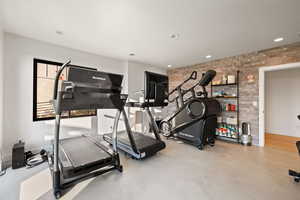 Exercise area with concrete flooring, brick wall, and recessed lighting