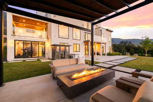 Back of house at dusk with a balcony, a yard, a patio area, stucco siding, and an outdoor living space with a fire pit