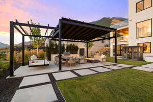 Patio terrace at dusk with a pergola, a mountain view, an outdoor fire pit, a patio, and a yard
