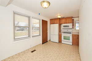 Kitchen featuring white appliances, light countertops, wood finish cabinetry, and light flooring