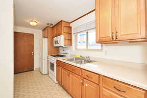 Kitchen with white appliances, light floors, light countertops, open shelves, and wood finish cabinets