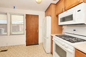 Kitchen with white appliances, light floors, wood finish cabinetry, and light countertops