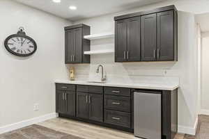 Bar area featuring open shelves, light stone countertops, light wood-style floors, stainless steel dishwasher, and recessed lighting