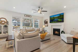 Living room featuring light wood-type flooring, a brick fireplace, ceiling fan, and recessed lighting
