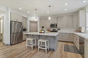 Kitchen with gray cabinets, a kitchen bar, stainless steel appliances, hanging light fixtures, and a kitchen island