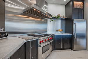 Kitchen featuring dark cabinetry, ventilation hood, high quality appliances, light tile patterned flooring, and modern cabinets