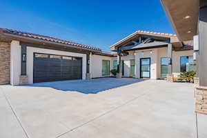 View of front of home with stone siding, a tile roof, stucco siding, and concrete driveway