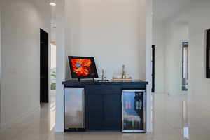 Indoor wet bar with beverage cooler, light tile patterned floors, stainless steel fridge, dark cabinets, and a high ceiling