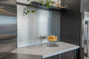 Kitchen view of elevator, stainless steel refrigerator, and light stone counters
