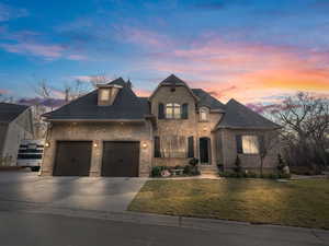 French provincial home with a lawn, driveway, a shingled roof, and brick siding