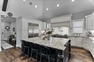Dual tone kitchen with light stone counters, backsplash, a kitchen breakfast bar, lofted ceiling, and dark wood-style floors