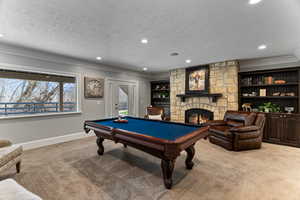 Game room featuring light colored carpet, ornamental molding, billiards table, a stone fireplace, and built in shelves