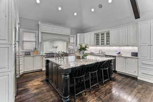Kitchen featuring light stone counters, lofted ceiling with beams, tasteful backsplash, two tone cabinetry, and a breakfast bar