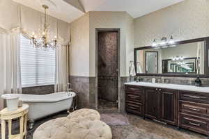 Full bath featuring vanity, a wainscoted wall, hanging lights, a freestanding tub, and a shower stall