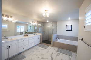 Full bath featuring a garden tub, double vanity, a textured ceiling, a stall shower, and light marble finish flooring