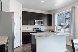 Kitchen with stainless steel appliances, light stone counters, dark wood-style flooring, an island with sink, and recessed lighting