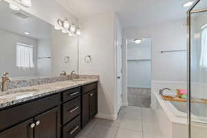 Full bathroom featuring a bath, double vanity, a spacious closet, light tile patterned flooring, and recessed lighting