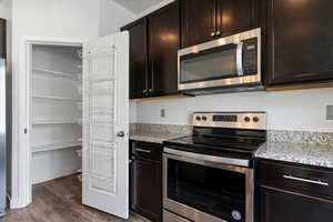 Kitchen with stainless steel appliances, light stone countertops, dark wood-type flooring, and dark wood finish cabinetry