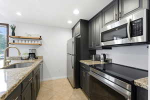 Kitchen featuring stainless steel appliances, open shelves, light stone counters, recessed lighting, and light tile patterned flooring
