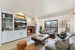 Living area featuring a brick fireplace, a textured ceiling, light tile patterned floors, built in shelves, and rail lighting