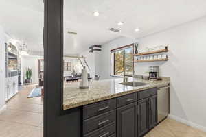 Kitchen with open shelves, a peninsula, light stone countertops, dishwasher, and light tile patterned floors