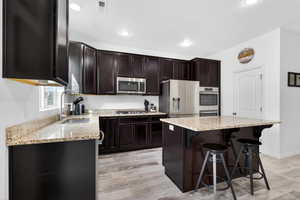 Kitchen featuring light stone counters, a kitchen bar, light wood-style flooring, stainless steel appliances, and a kitchen island