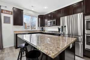 Kitchen featuring stainless steel appliances, a kitchen bar, light stone counters, a kitchen island, and recessed lighting