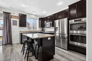 Kitchen with stainless steel appliances, a breakfast bar, a kitchen island, light wood-type flooring, and recessed lighting