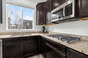 Kitchen with dark wood finish cabinets, stainless steel appliances, and light stone countertops