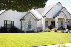 View of front facade with board and batten siding, a front lawn, brick siding, and a porch