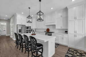 Kitchen with a kitchen breakfast bar, white cabinetry, premium appliances, a kitchen island, and light wood finished floors