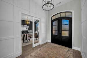 Entrance foyer with french doors, a chandelier, a decorative wall, and wood finished floors
