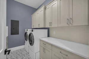 Laundry area with electric panel, washing machine and dryer, cabinet space, and light tile patterned flooring